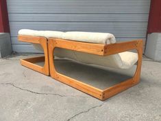 a wooden bench with a white cushion on the top and bottom part, sitting in front of a garage door