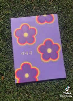 a purple book with flowers painted on the cover is laying in the grass and it's numbers are 444