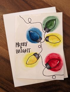 a card with christmas lights on it sitting on top of a wooden table next to a piece of paper