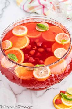 a glass bowl filled with liquid and sliced oranges on top of a marble table