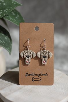 a pair of earrings with a dog's head on it sitting next to a potted plant