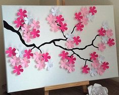 a white canvas with pink and white paper flowers on it sitting on a wooden easel