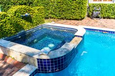 an outdoor swimming pool surrounded by shrubbery and stone pavers, with blue tiles on the edge