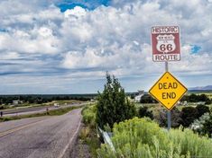 a street sign on the side of a road with clouds in the sky behind it