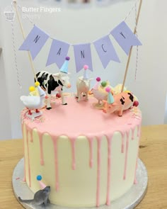 a birthday cake decorated with farm animals and bunting flags on a wooden table in front of a white wall