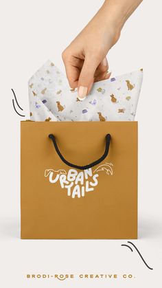 a hand holding a brown paper bag with the words urban tails printed on it