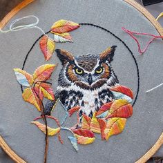 an embroidered owl with yellow eyes sits in a circle surrounded by autumn leaves and thread