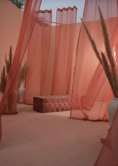 an outdoor area with sheer curtains and vases on the floor, in front of pink walls