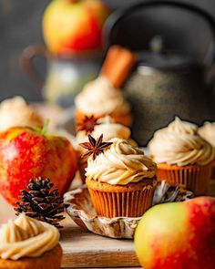 cupcakes with frosting, cinnamon and an apple next to them on a cutting board