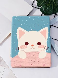 a white cat with big eyes sitting on top of a blue and pink notebook cover