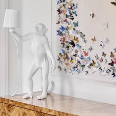 a white monkey lamp sitting on top of a dresser next to a wall with butterflies