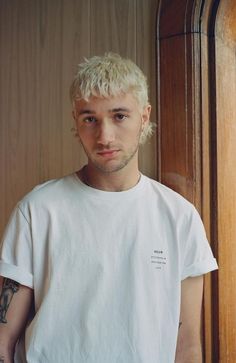 a man with blonde hair and tattoos standing in front of a wooden door