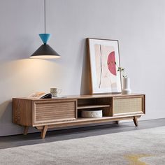 a wooden entertainment center with an art print on the wall next to it and a lamp