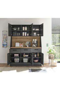 a kitchen with black cabinets and shelves filled with dishes on top of each shelf, next to a potted plant