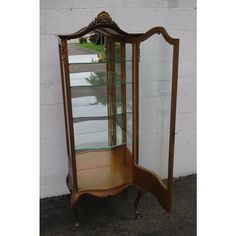 an antique china cabinet with glass doors and wood trimmings on the top, in front of a white brick wall