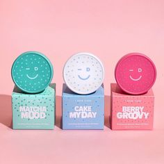 three boxes with different types of cake in them on a pink background and one has a smiley face