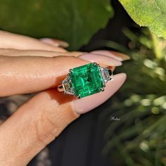 a woman's hand holding an emerald and diamond ring