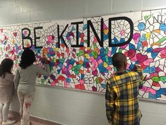 three people are standing in front of a wall that says be kind