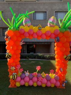 an arch made out of balloons and decorations in the shape of flowers, bees, and pineapples