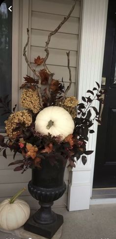 a white pumpkin sitting on top of a black vase filled with leaves and flowers next to a door