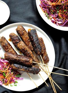 several skewers of meat on a plate with coleslaw and carrot slaw