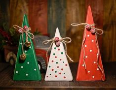 three wooden christmas trees with bows and bells on them, one painted red, the other green