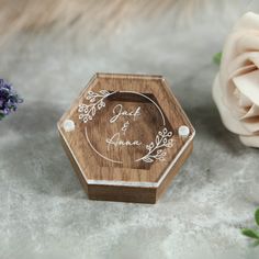 a wooden ring box with a wedding date engraved on the lid and flowers next to it