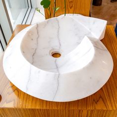 a white marble sink sitting on top of a wooden counter next to a plant in a vase