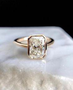 a close up of a diamond ring on a marble slab with white and gold accents