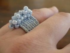 a crocheted ring with blue beads on it's middle finger is held in someone's hand