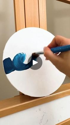 a person is using a marker to paint the bottom of a white object with blue swirls