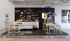 a room with tables, chairs and shelves filled with plants on the wall behind them