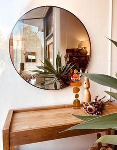 a round mirror on the wall above a wooden table with plants and vases in front of it