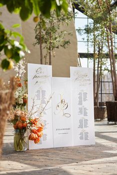 flowers in a vase sitting on the ground next to two wedding program booklets with gold lettering