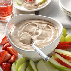 a bowl of dip surrounded by sliced apples and strawberries