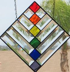 a multicolored stained glass window hanging from a chain with a palm tree in the background