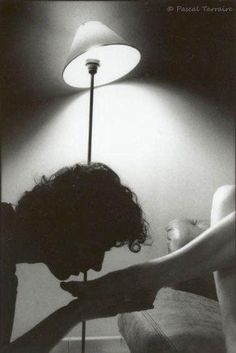 a black and white photo of a woman leaning on a table next to a lamp