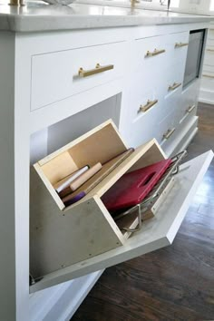 an open drawer on the side of a white kitchen counter with drawers and other items in it