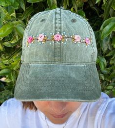 a woman wearing a green hat with pink roses on the front and blue flowers on the back