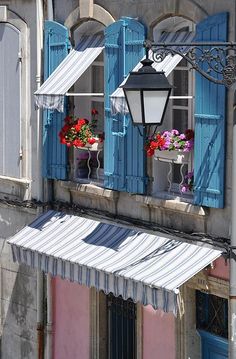 an old building with blue shutters and flower boxes on the window sill in front of it