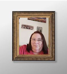 a woman with glasses is looking at the camera in front of a white wall and gold frame