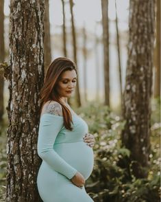 a pregnant woman leaning against a tree in the woods