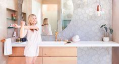 a woman standing in front of a bathroom mirror with her arms spread out to the side