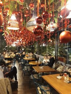 people sitting at tables in a restaurant with hanging lights and decorations on the ceiling above them