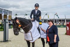 a woman standing next to a horse with a jockey on it's back and holding the reins