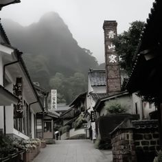 a narrow street with buildings and mountains in the background on a foggy day,