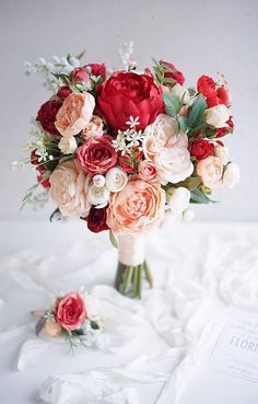 a bouquet of flowers sitting on top of a white cloth covered tablecloth next to a book