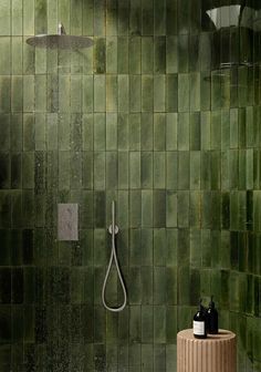 a green tiled bathroom with a shower head and soap dispenser next to it