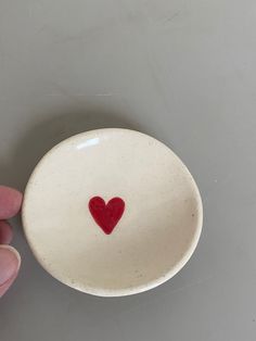 a hand holding a white bowl with a red heart on it