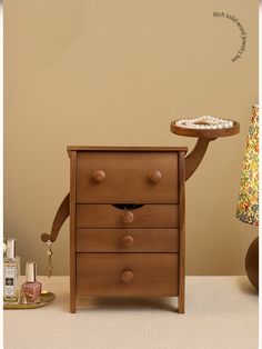 a wooden dresser with two drawers and a tray on it's legs, in front of a beige wall